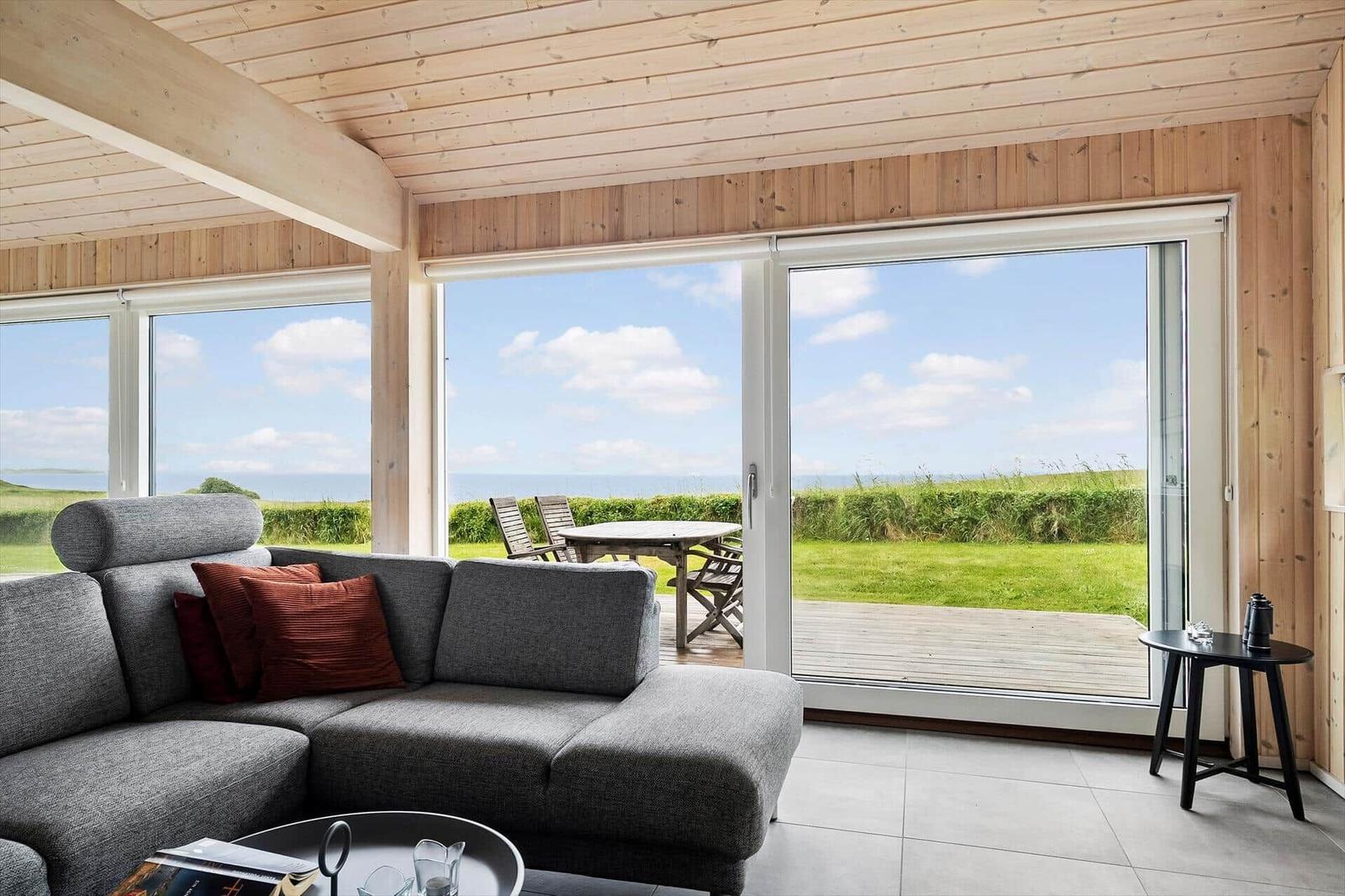 Wohnzimmer mit Sofa, Terrasse und Meerblick durch große Fenster.