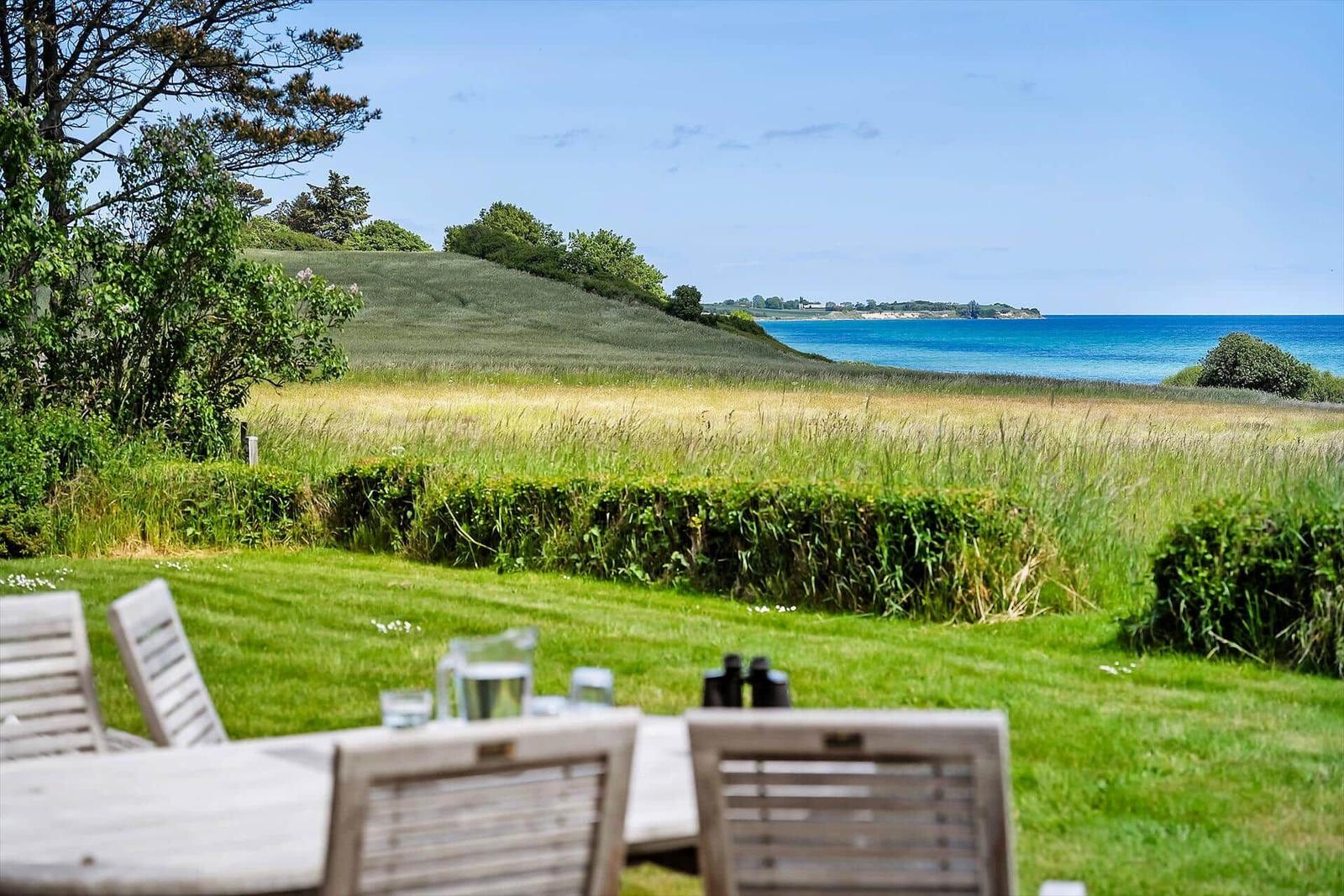 Terrasse mit Tisch und Stühlen, Blick auf Grasland und Meer.