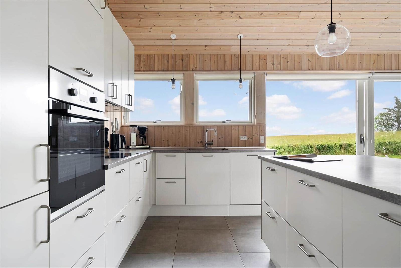 Moderne Küche mit weißen Schränken, Holzdecke und Blick auf grünes Feld.