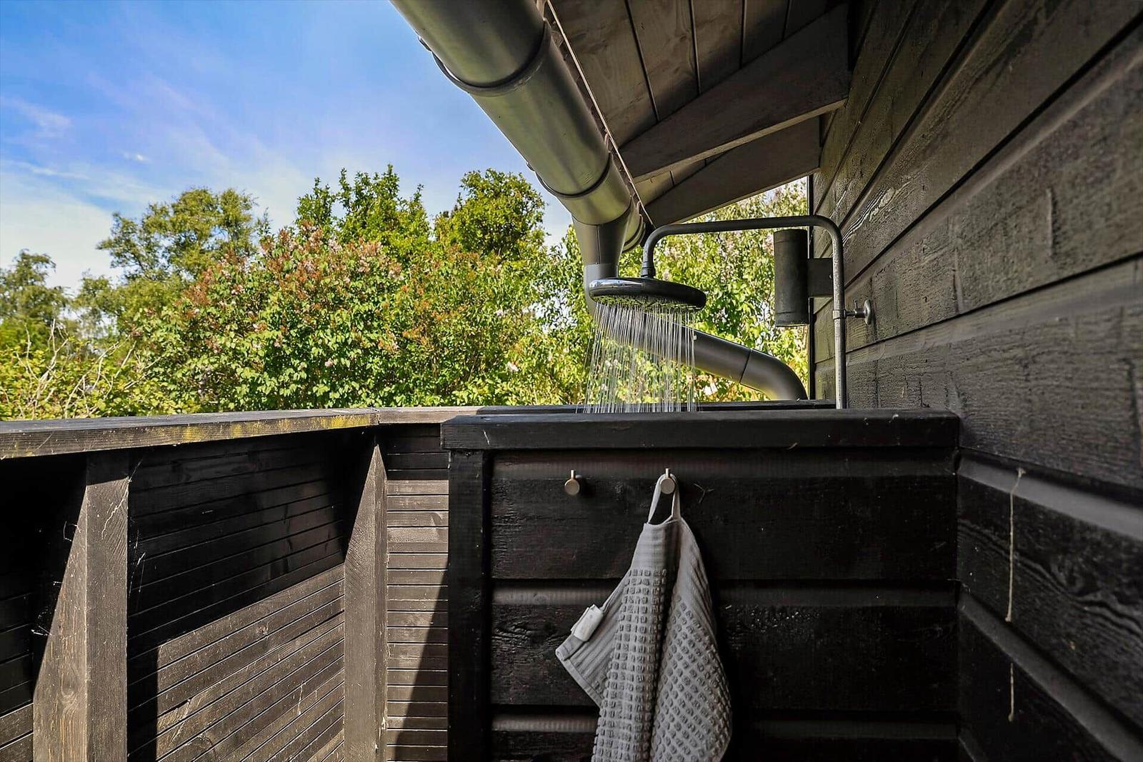Außendusche mit Dachüberstand und Blick auf grüne Bäume.
