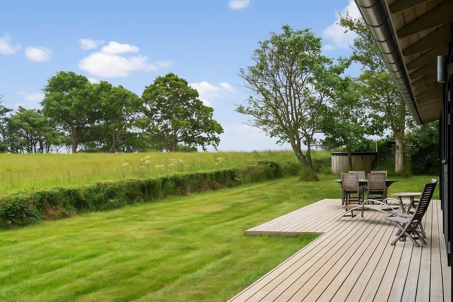 Terrasse mit Sitzgelegenheiten und Blick auf grünes Feld und Bäume.