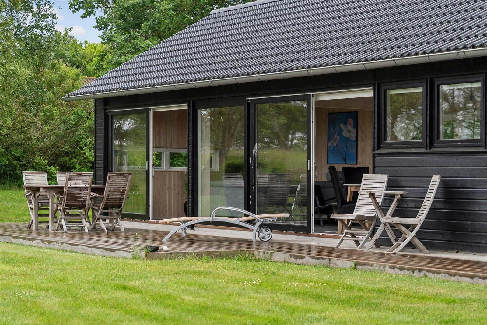 Moderne Holzhütte mit Terrasse, Gartenmöbeln und Blick in den Innenraum.