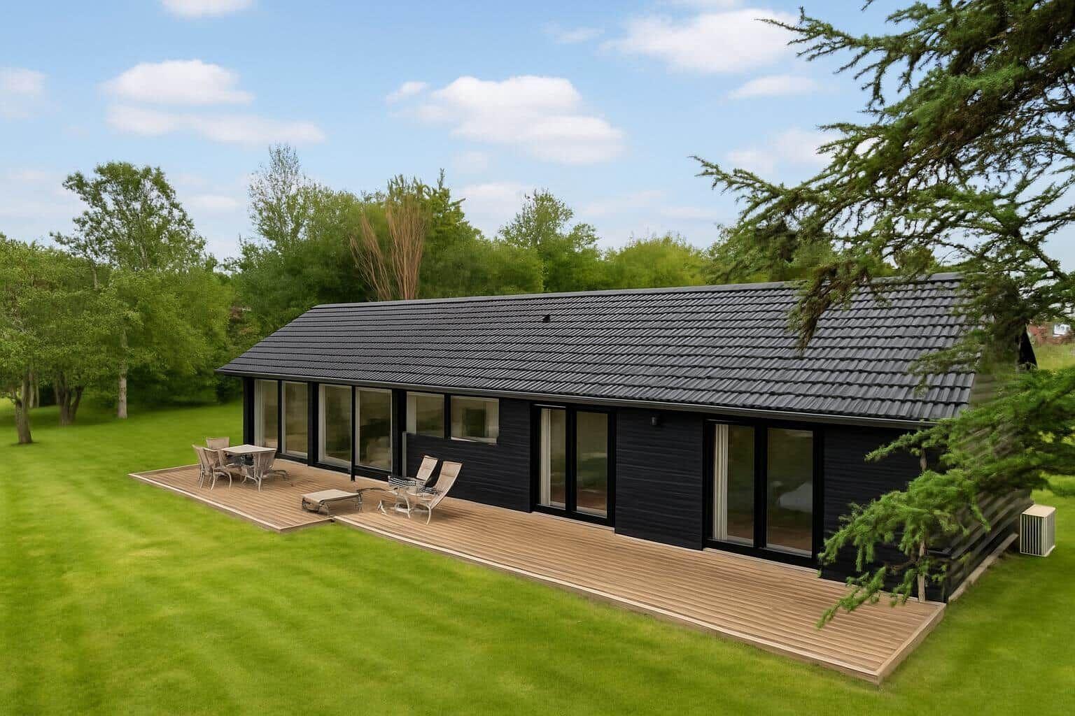 Moderne schwarze Hütte mit Terrasse und Garten. Große Fensterfront mit Sitzgelegenheiten.