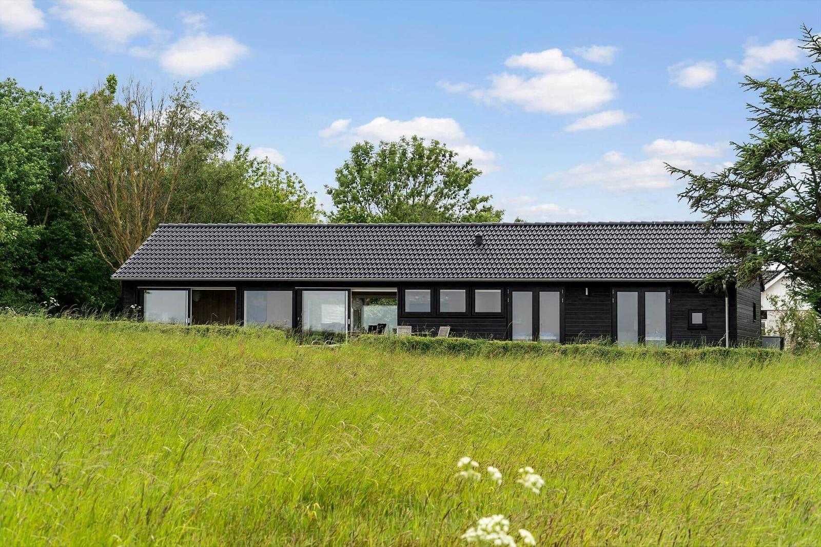 Moderne schwarze Hütte mit Glasfronten in grüner Landschaft unter blauem Himmel.