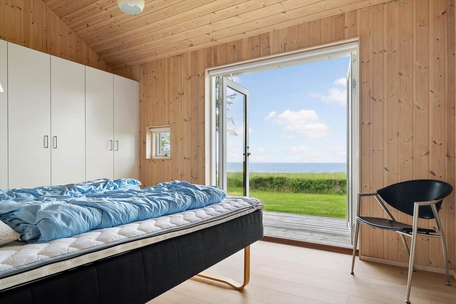 Schlafzimmer mit Blick auf Meer, Bett, Stuhl und Schrank.