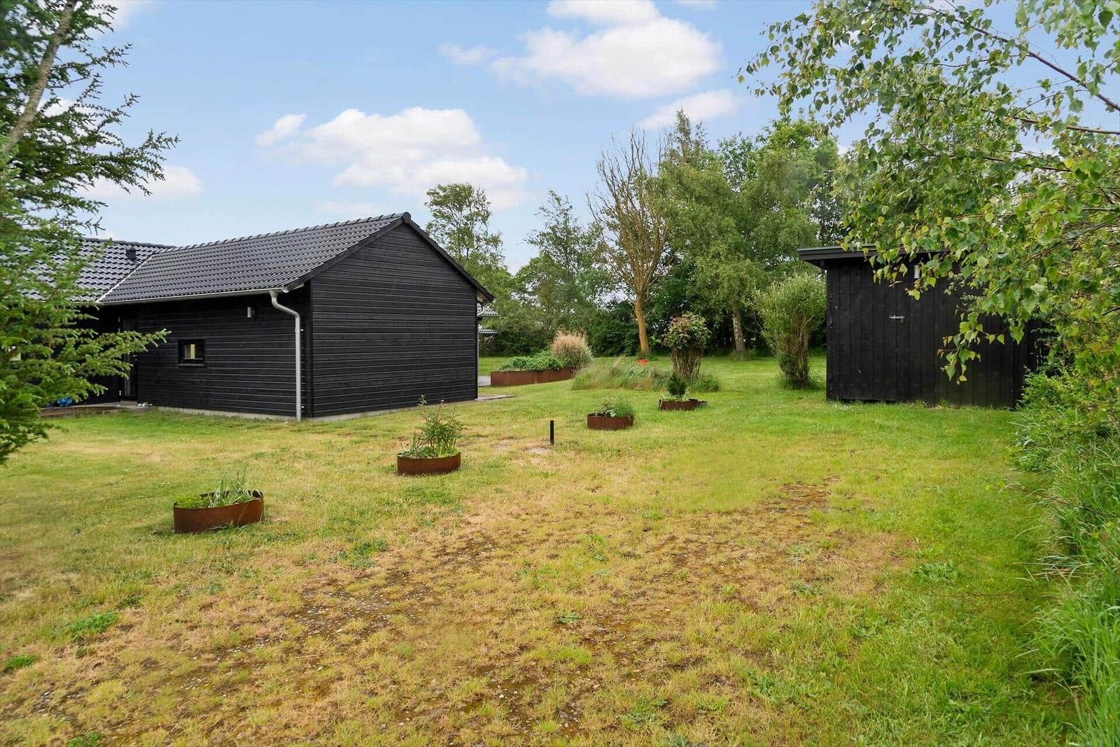 Schwarzes Haus mit Garten und kleinem Nebengebäude unter blauem Himmel.