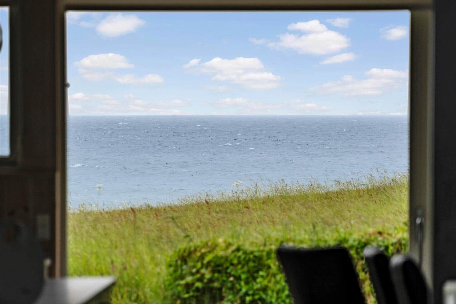 Durch das Fenster ist das Meer und eine grüne Wiese zu sehen.