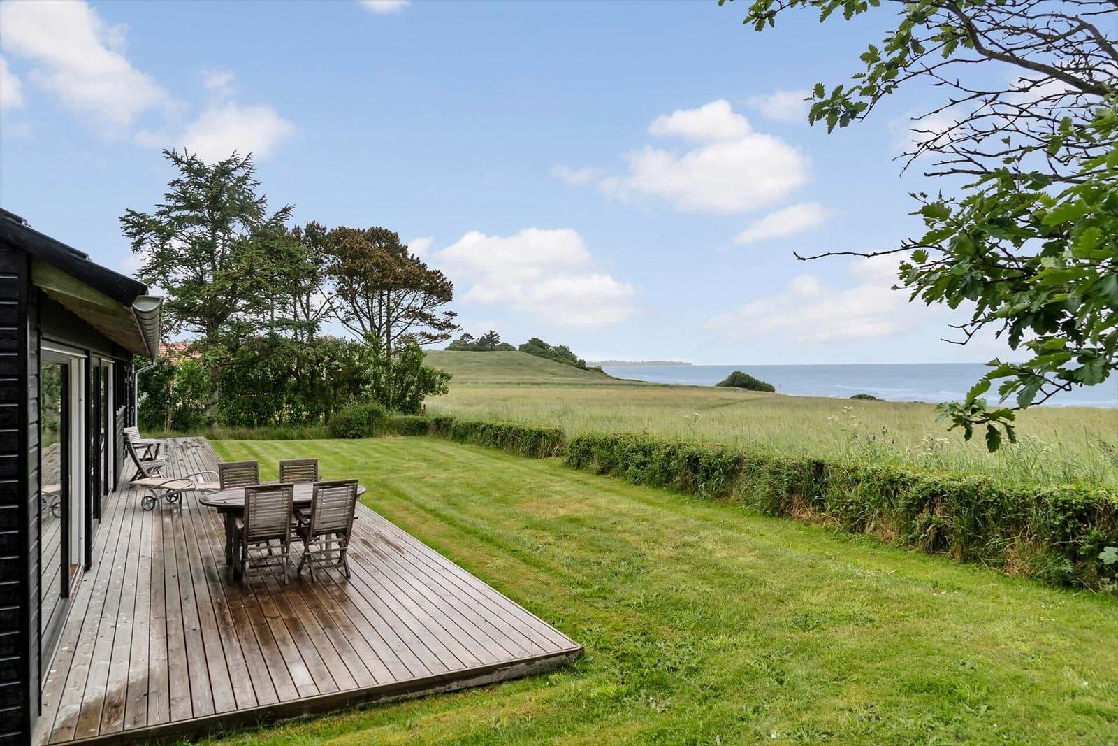 Terrasse mit Tisch und Stühlen, Blick auf Grünland und Meer.