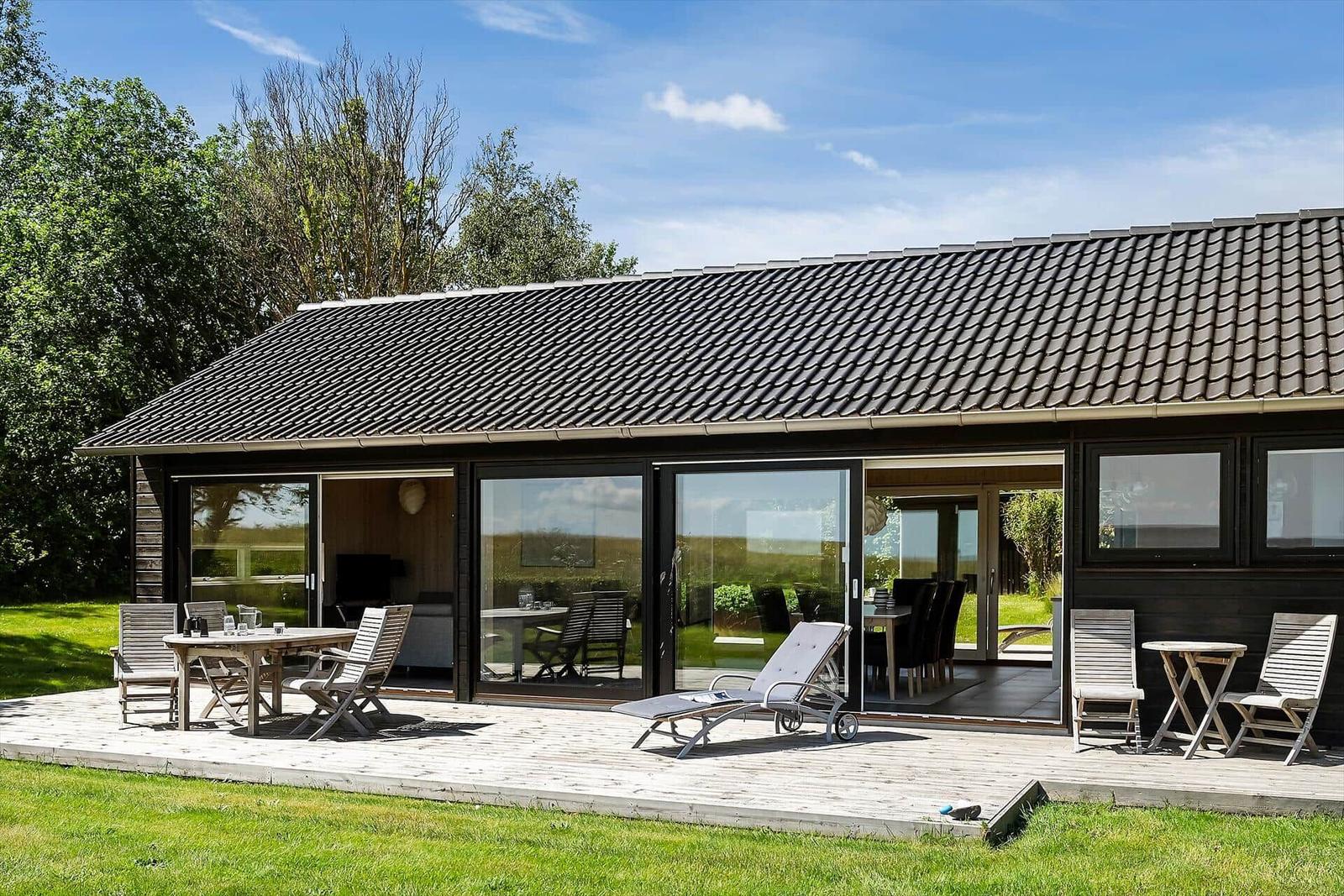 Moderne Villa mit Terrasse, Sitzgelegenheiten und großem Glasbereich. Grün umgeben.