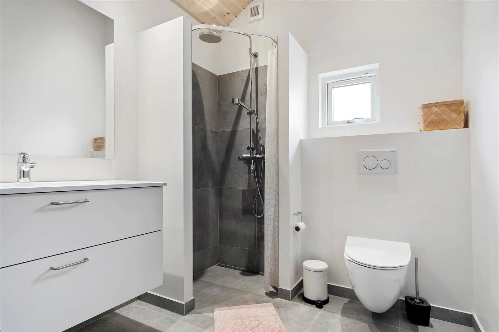 Badezimmer mit Dusche, Waschbecken und Toilette. Holzdecke und Fenster.