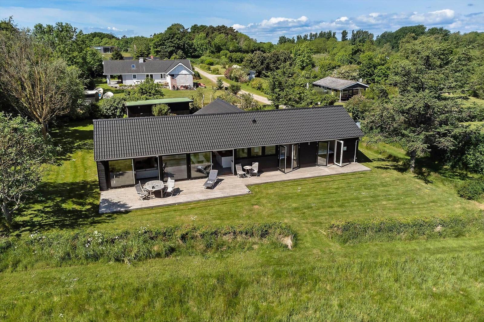 Moderne Villa mit großem Holzterrasse und Garten. Umgeben von Bäumen und Grünflächen.