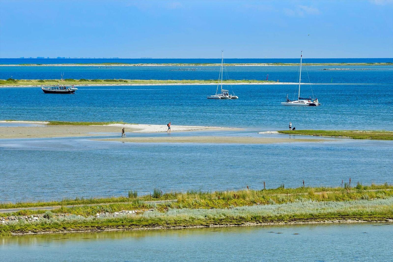 Sailboats und Personen an einem sandigen Strand bei ruhigem Wasser.