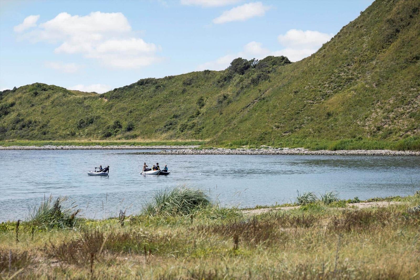 Zwei Boote mit Personen auf ruhigem Wasser vor grünen Hügeln.