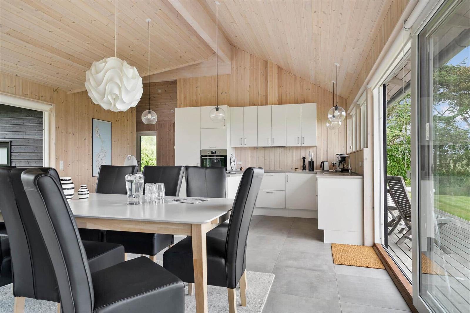 Essbereich mit Tisch und Stühlen, Küche und Terrasse mit Blick auf Grünflächen.