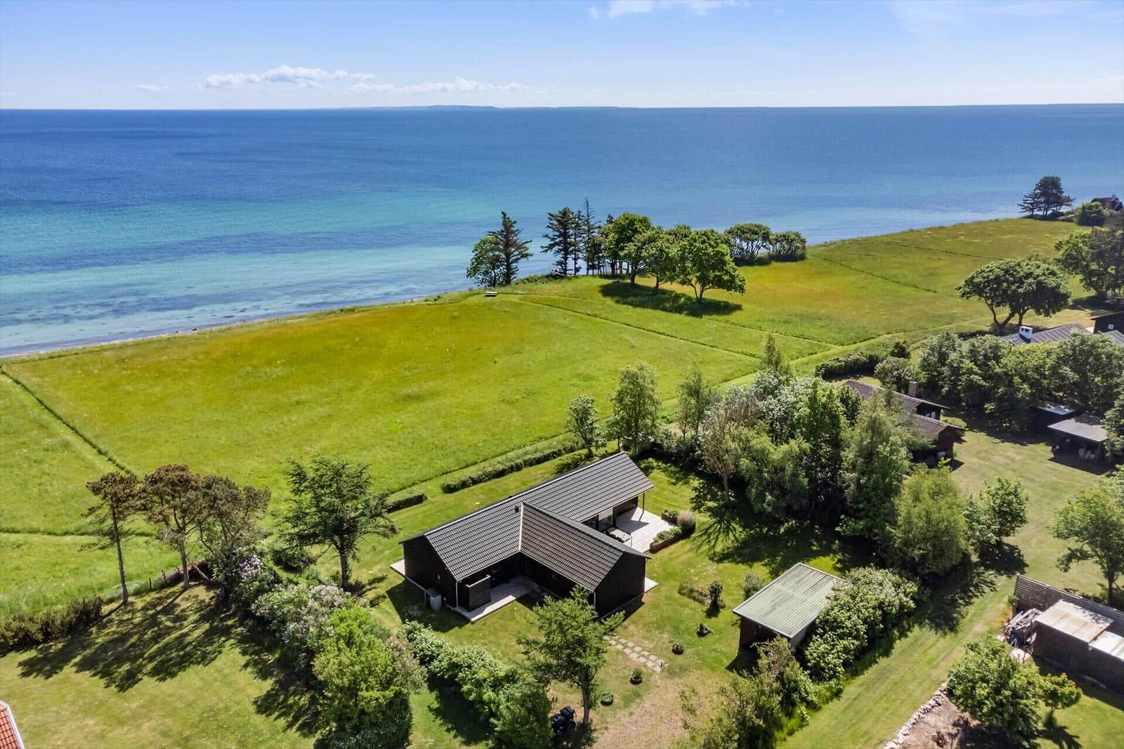 Haus mit Garten und Meerblick. Grünfläche, Bäume und Strand sind sichtbar.