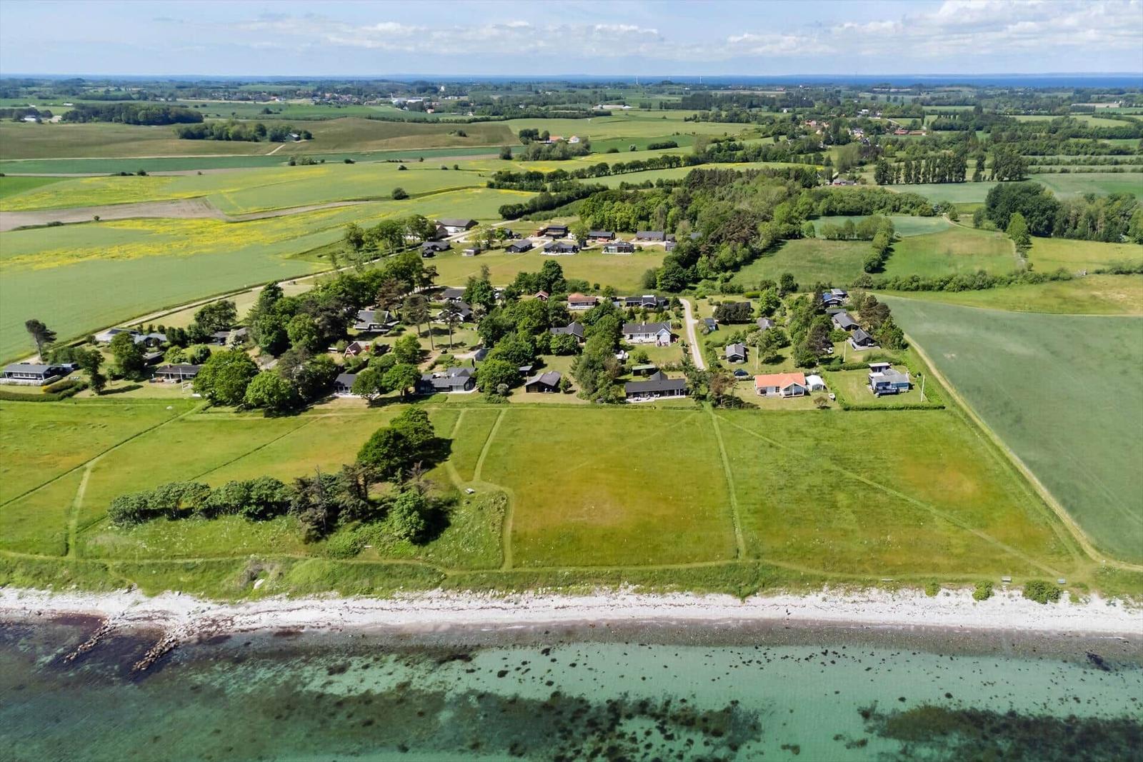 Aerial view of a coastal village with green fields and scattered houses near the sea.