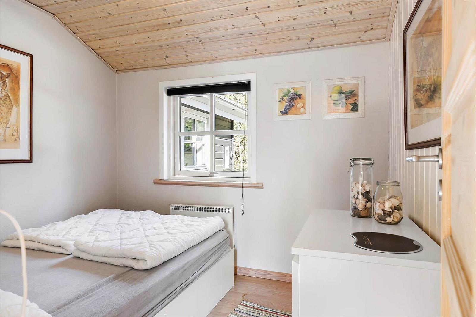 Schlafzimmer mit Bett, Fenster und dekorativen Bildern an der Wand.