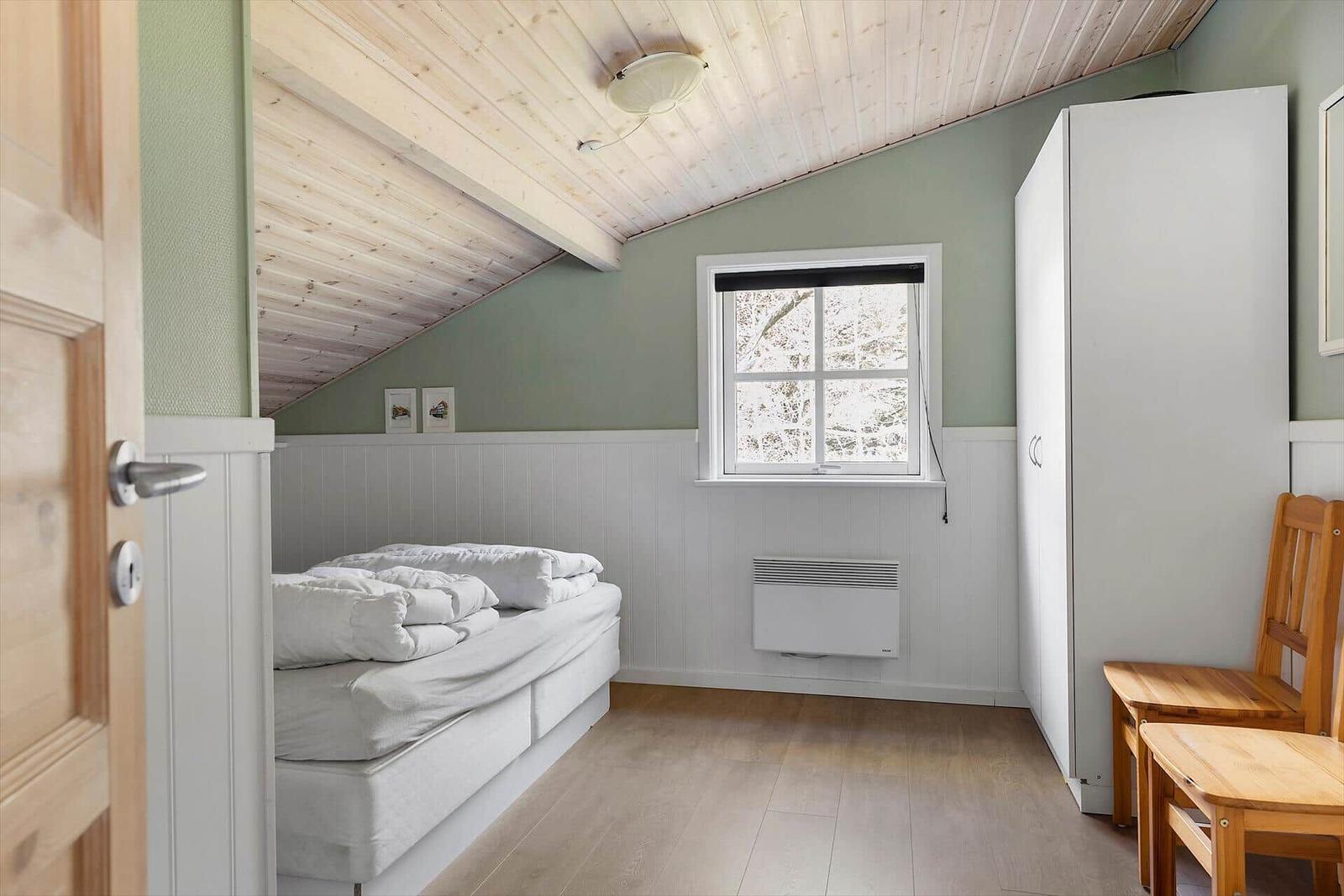 Schlafzimmer mit Bett, Fenster und Kleiderschrank unter schrägem Dach.