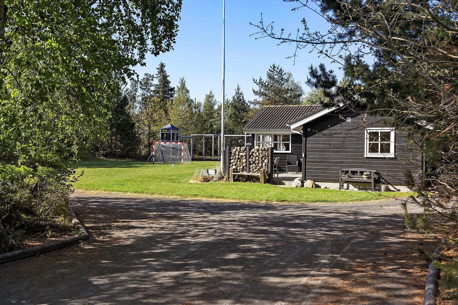 Ein schwarzes Haus mit Garten, Spielplatz und Holzstapel.
