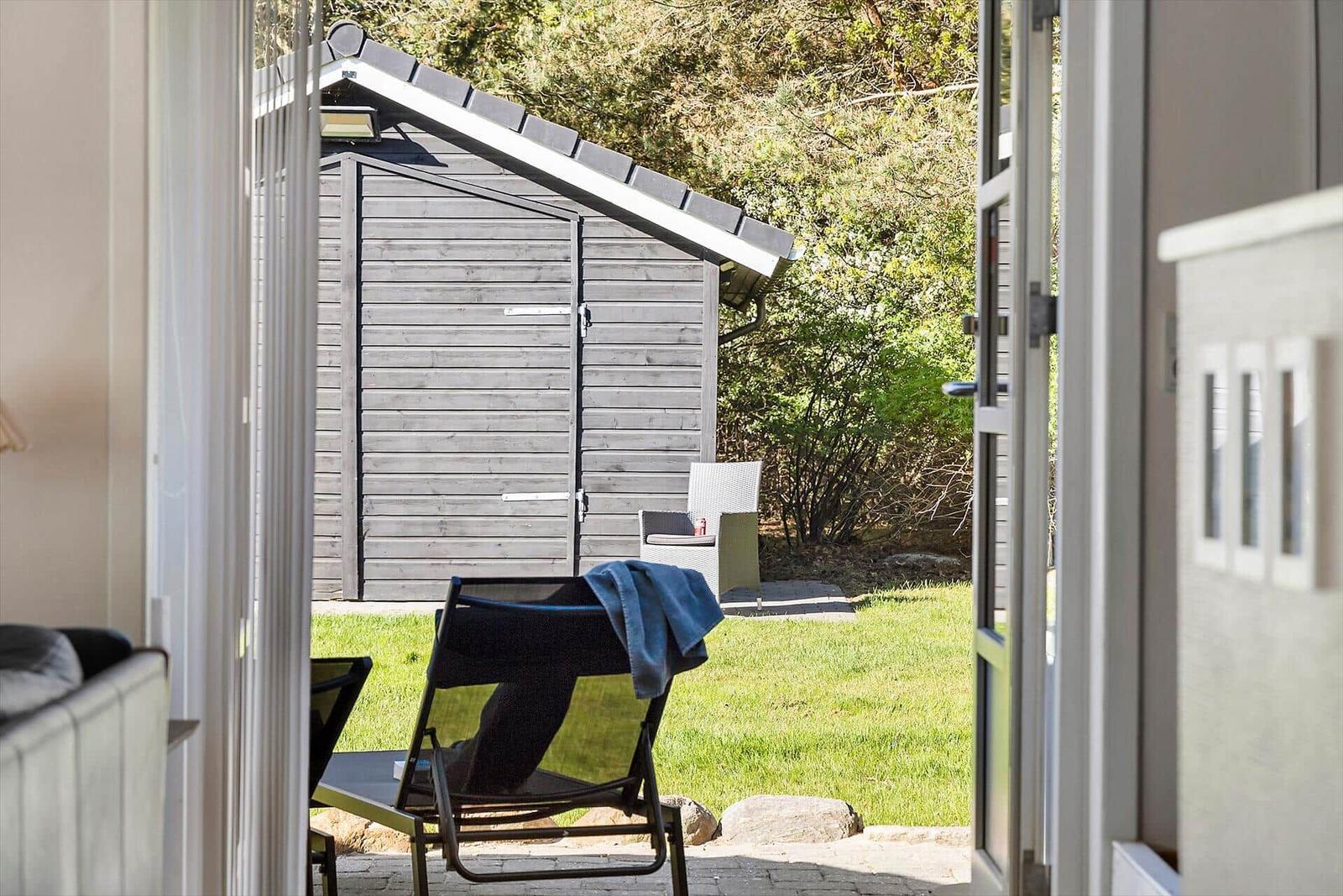 Durch die Tür blickt man auf eine Terrasse mit Liegestühlen und einen Holzschuppen im Garten.