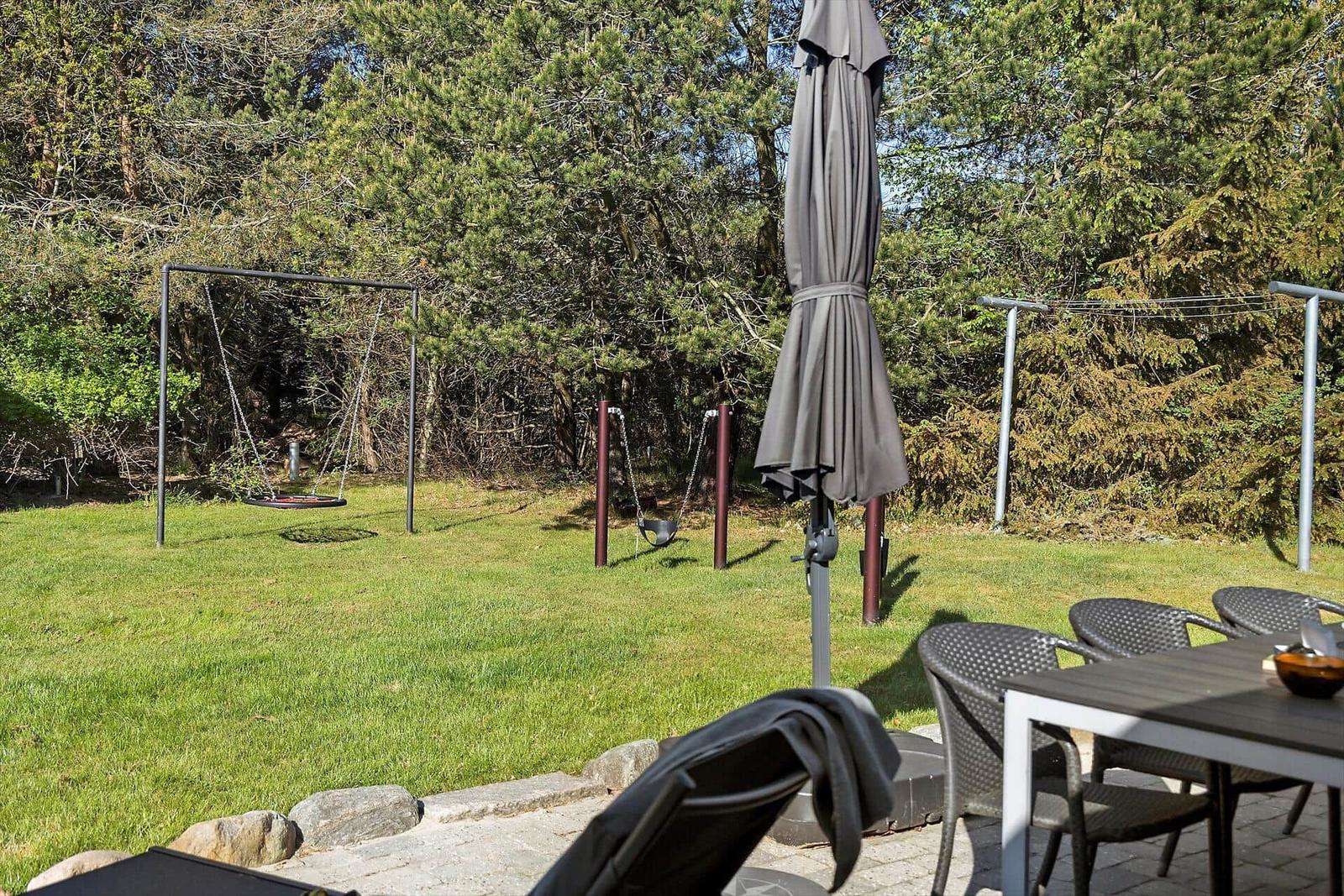 Garten mit Spielplatz, Tisch, Stühle und geschlossenem Sonnenschirm.
