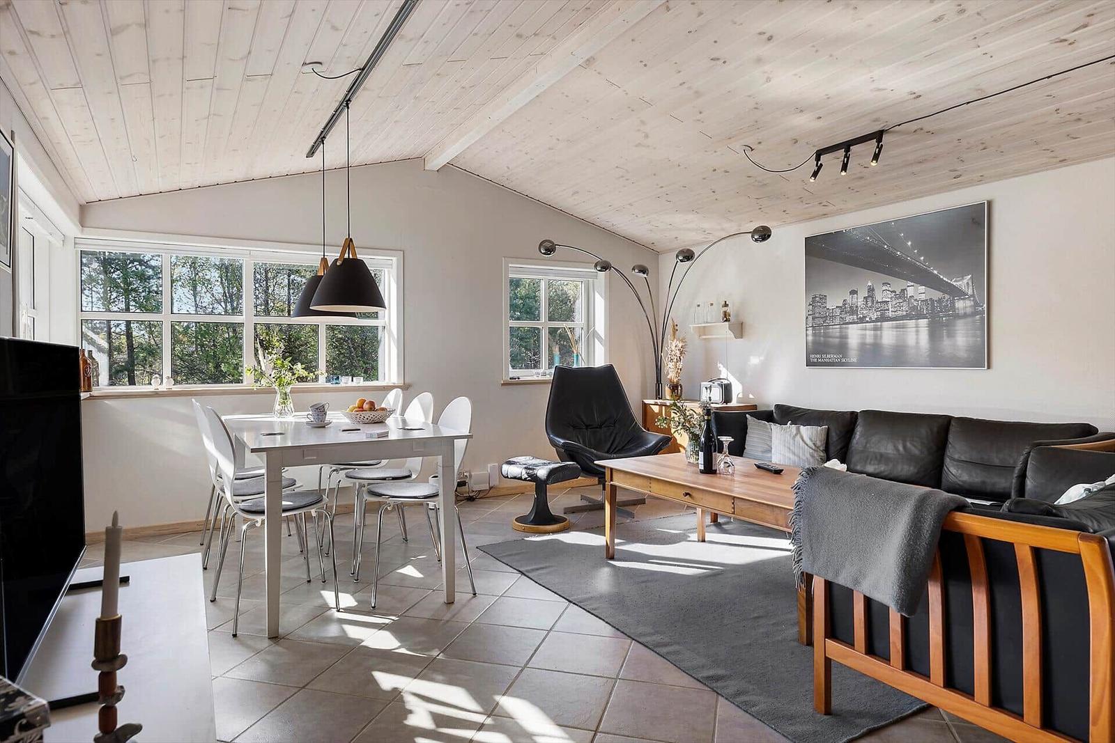 Wohn- und Essbereich mit Holzdecke, Sofa, Tisch und Fenstern.