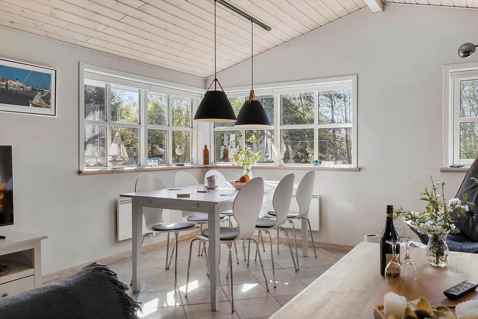 Essbereich mit Tisch, Stühlen und Fenstern. Decke aus Holz, schwarze Hängelampen.
