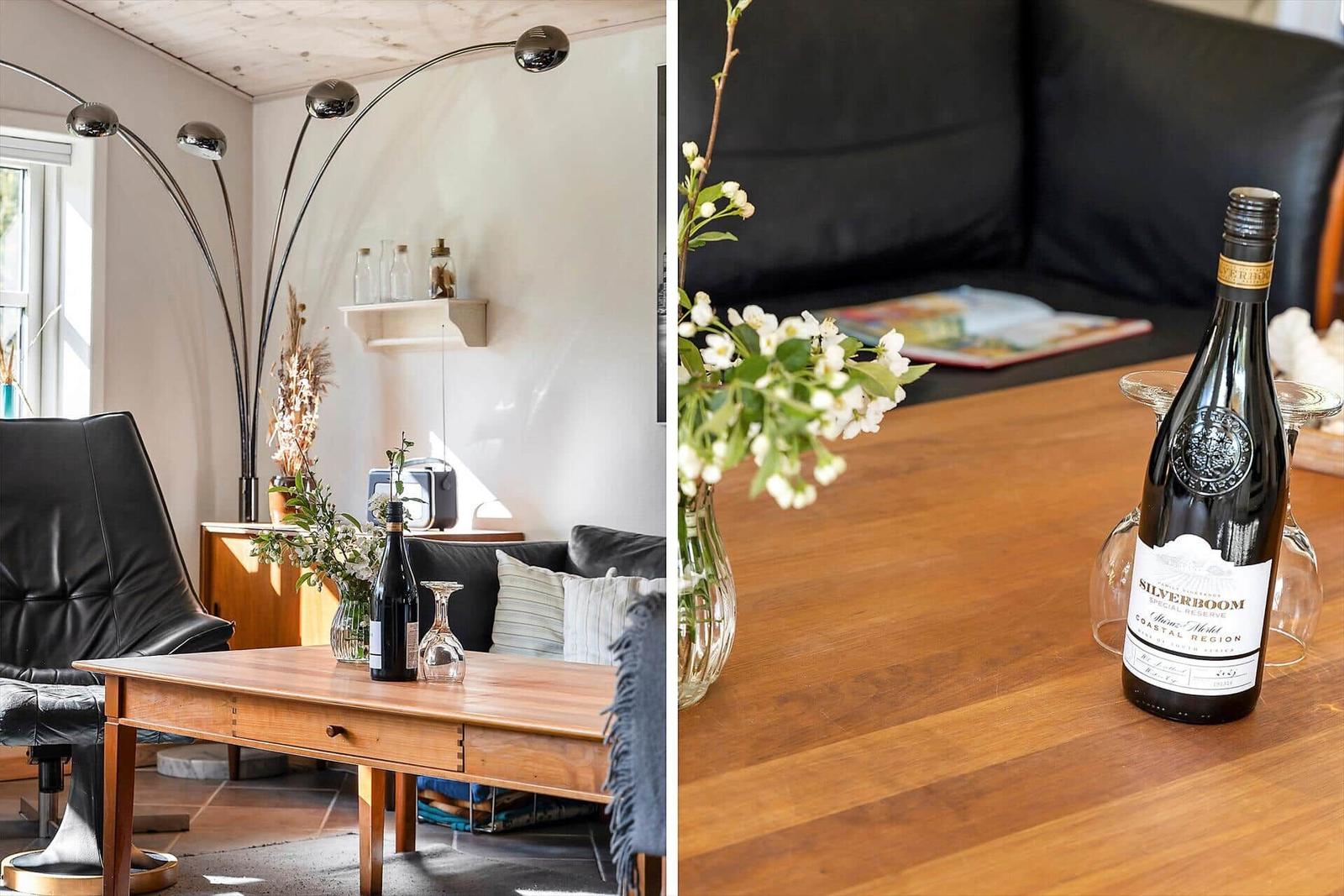 Holztisch mit Weinflasche und Blumen vor dunklem Sofa