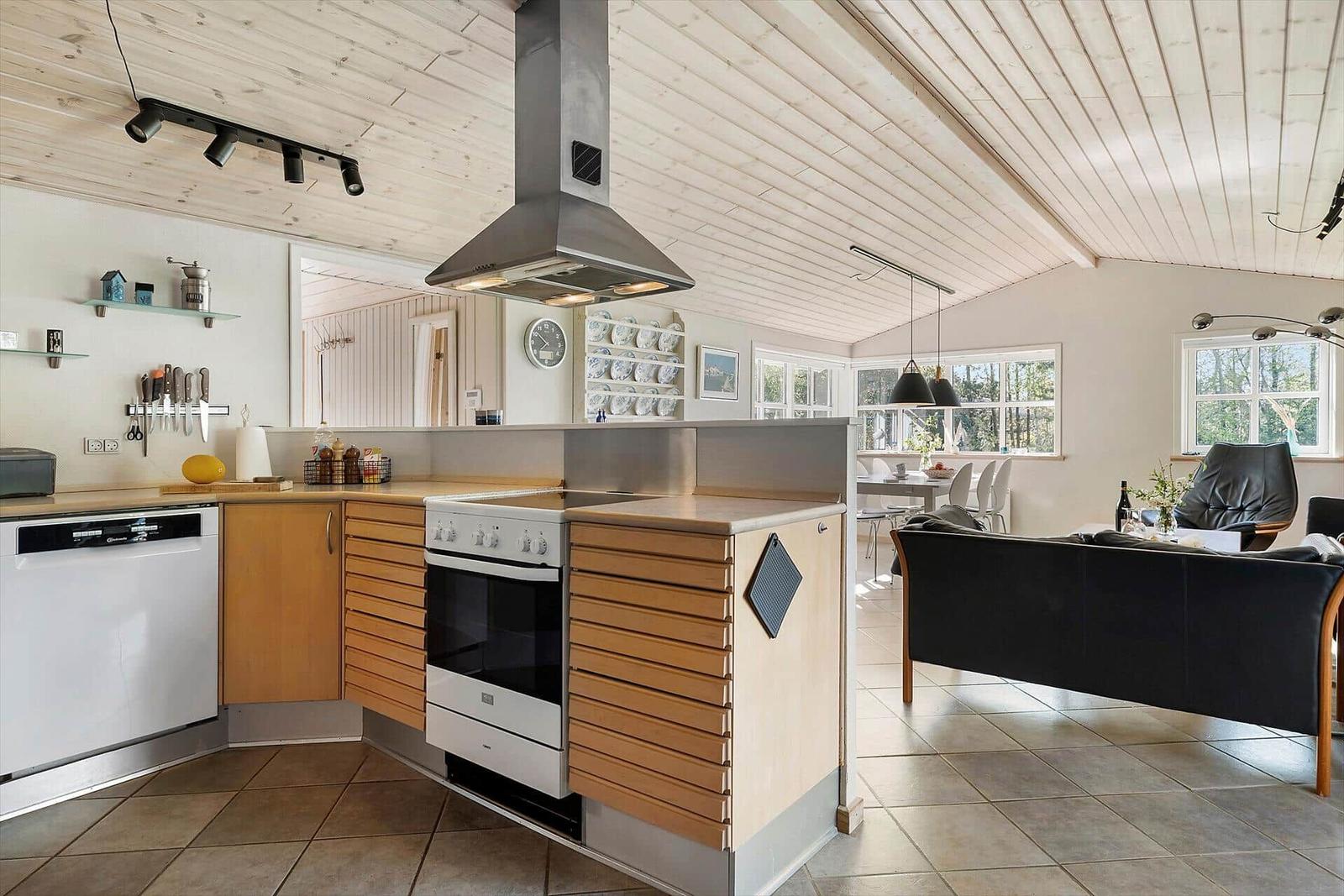 Küche mit Holzschrank und Edelstahlherd, angrenzendes Wohnzimmer mit Sofa und Tisch.