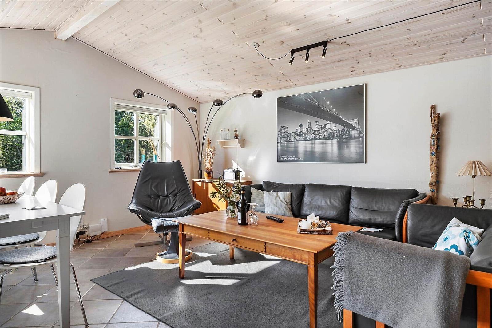 Wohnzimmer mit Sofa, Couchtisch und Essbereich unter Holzdecke.