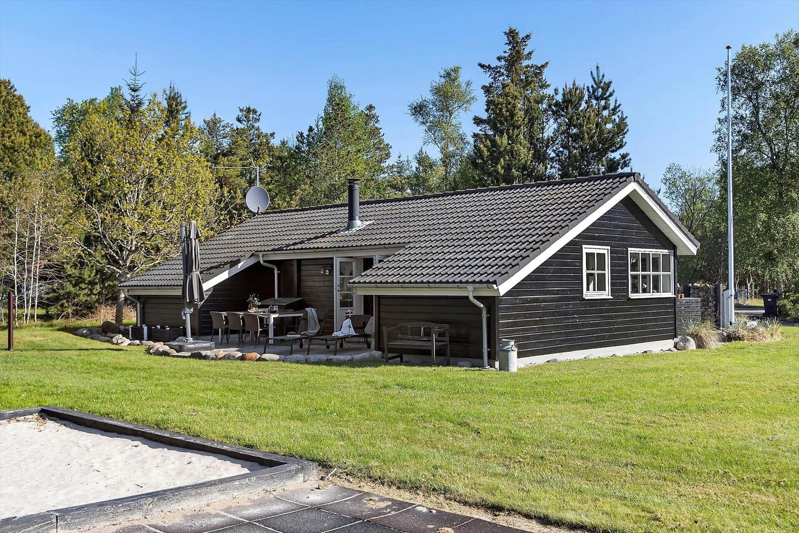 Holzhaus mit Terrasse, Grill und Garten. Umgeben von Bäumen und Gras.