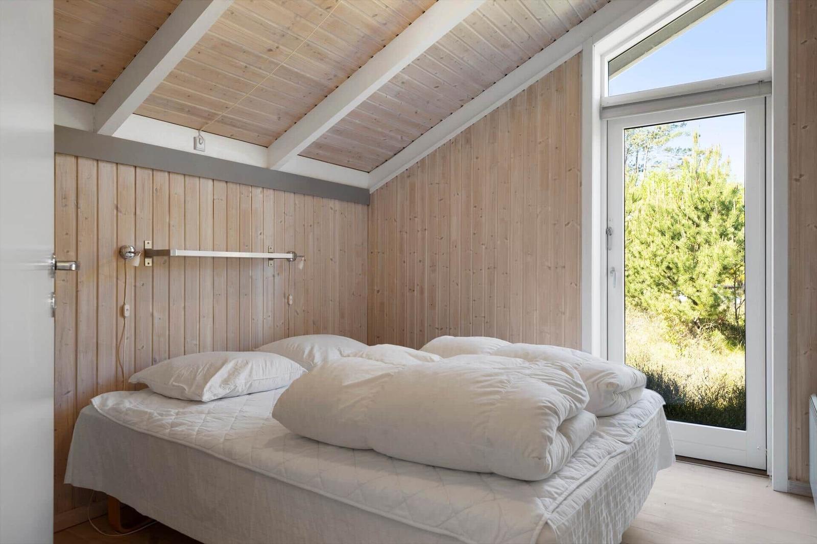 Bedroom with wooden walls and double bed. Window with view of greenery.