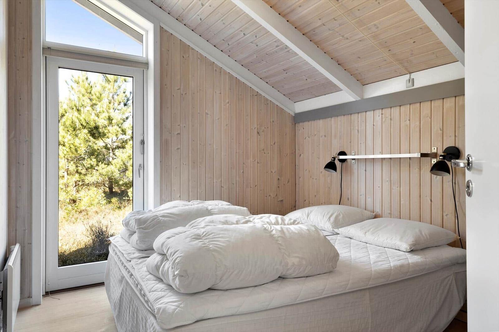 Bedroom with bed, wooden walls, and forest view through window.