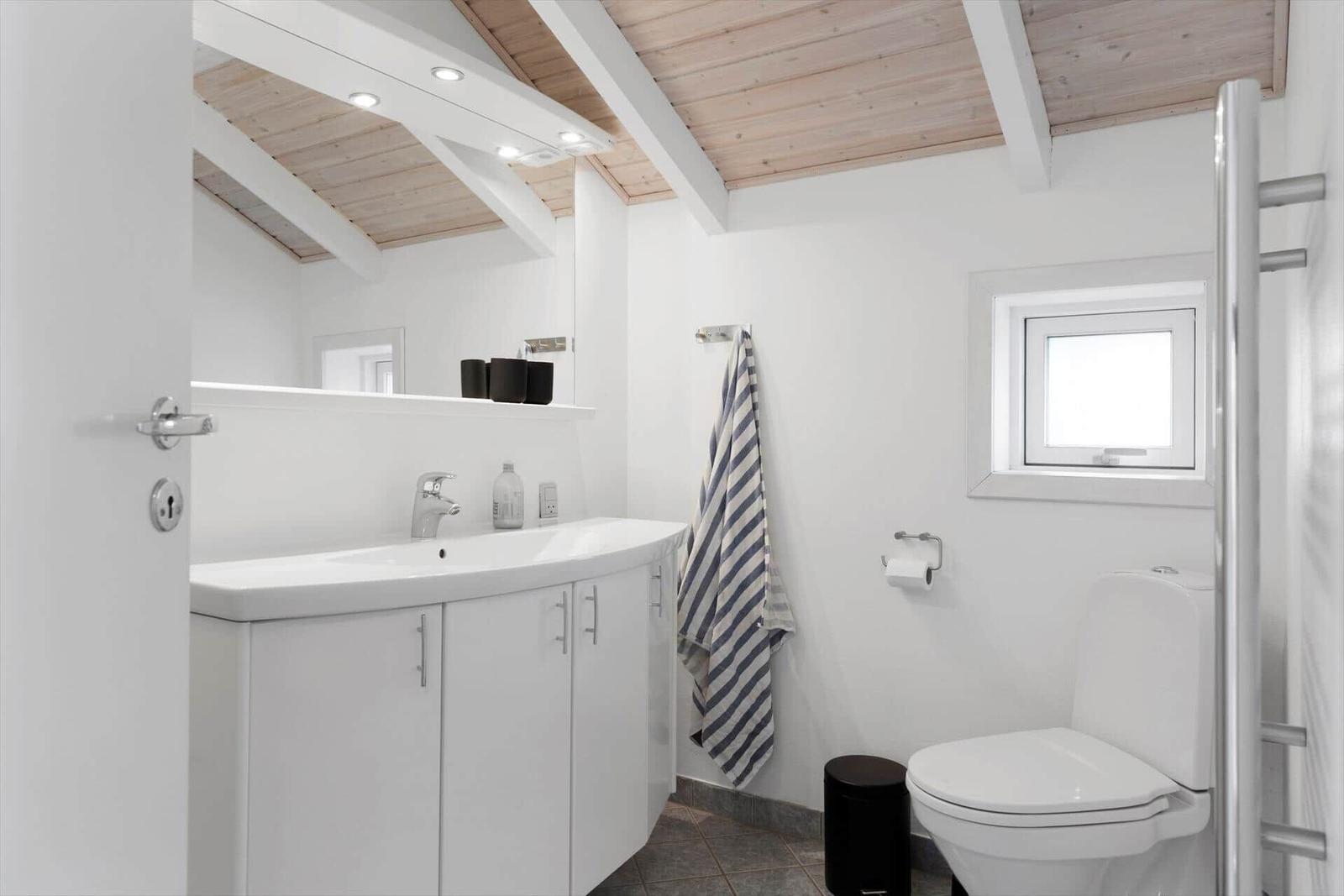 Bathroom with sink, toilet, and shower under wooden ceiling.