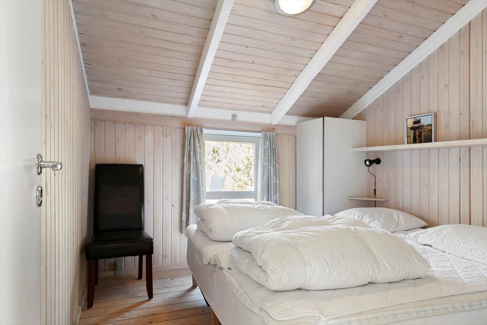 Bedroom with bed, wardrobe, and chair against wooden walls.