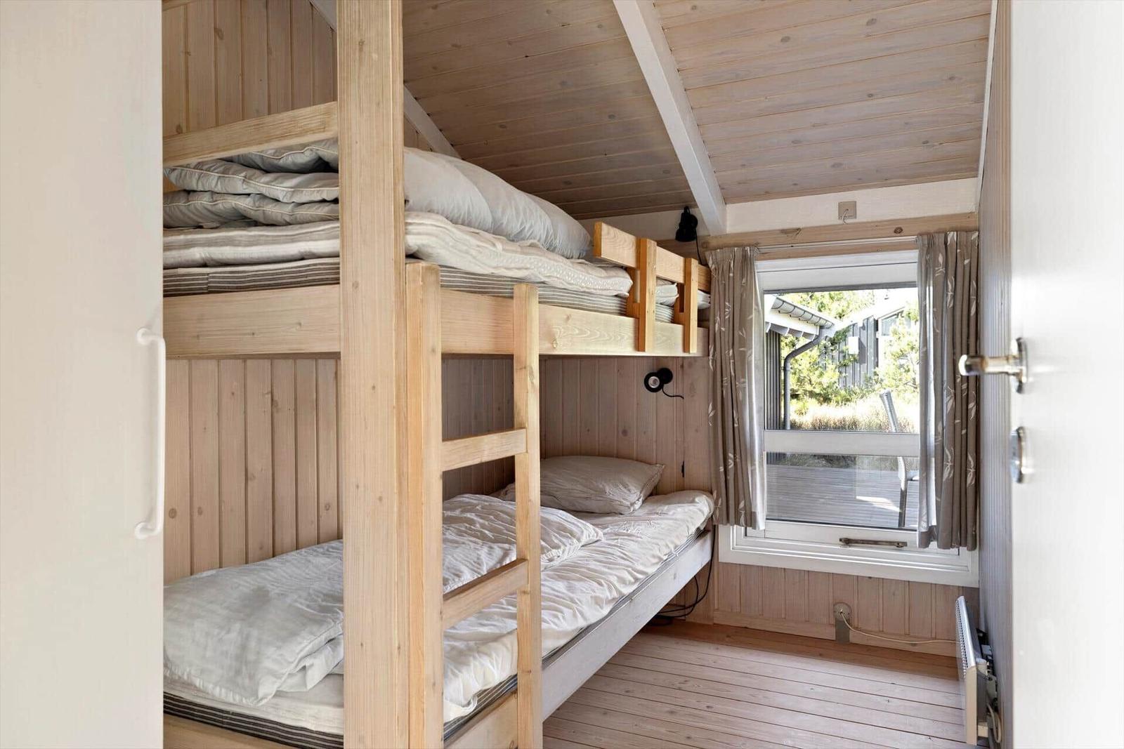 Room with bunk bed, wooden walls, and window with view outside.