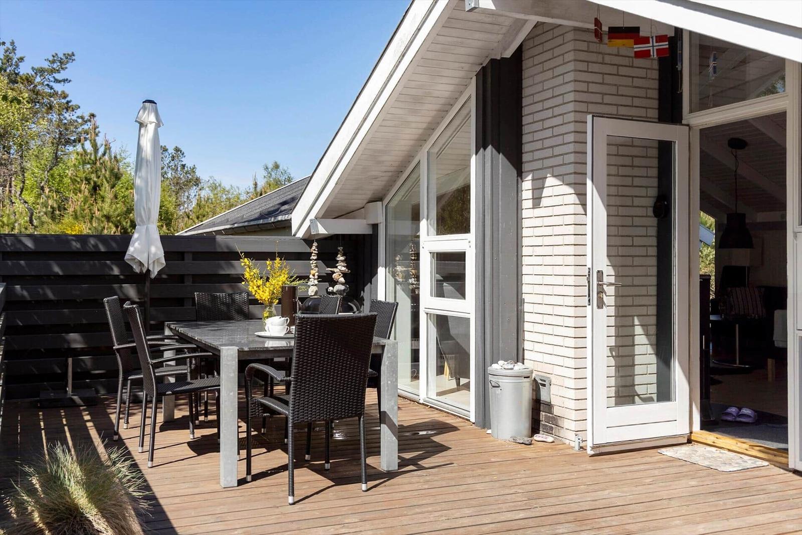 Deck with table, chairs, and umbrella. Glass doors lead into the house.