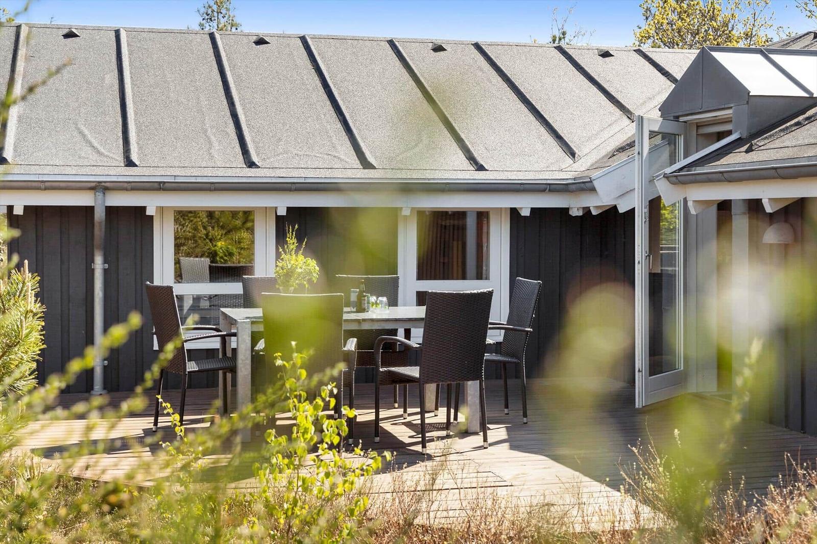 Deck with table and chairs in front of a house with dark siding and gray roof.
