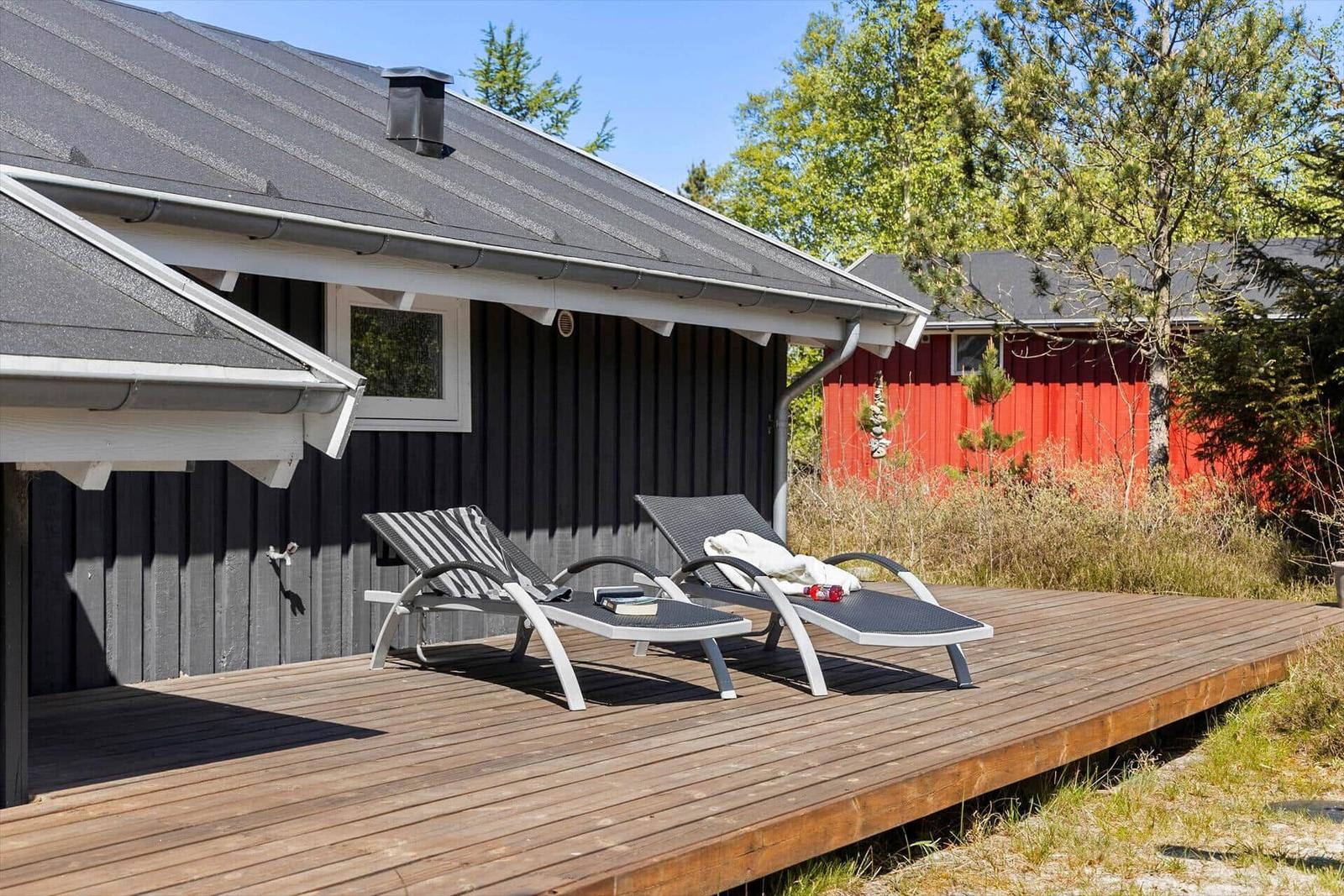 Deck with two lounge chairs in front of a house with dark siding.
