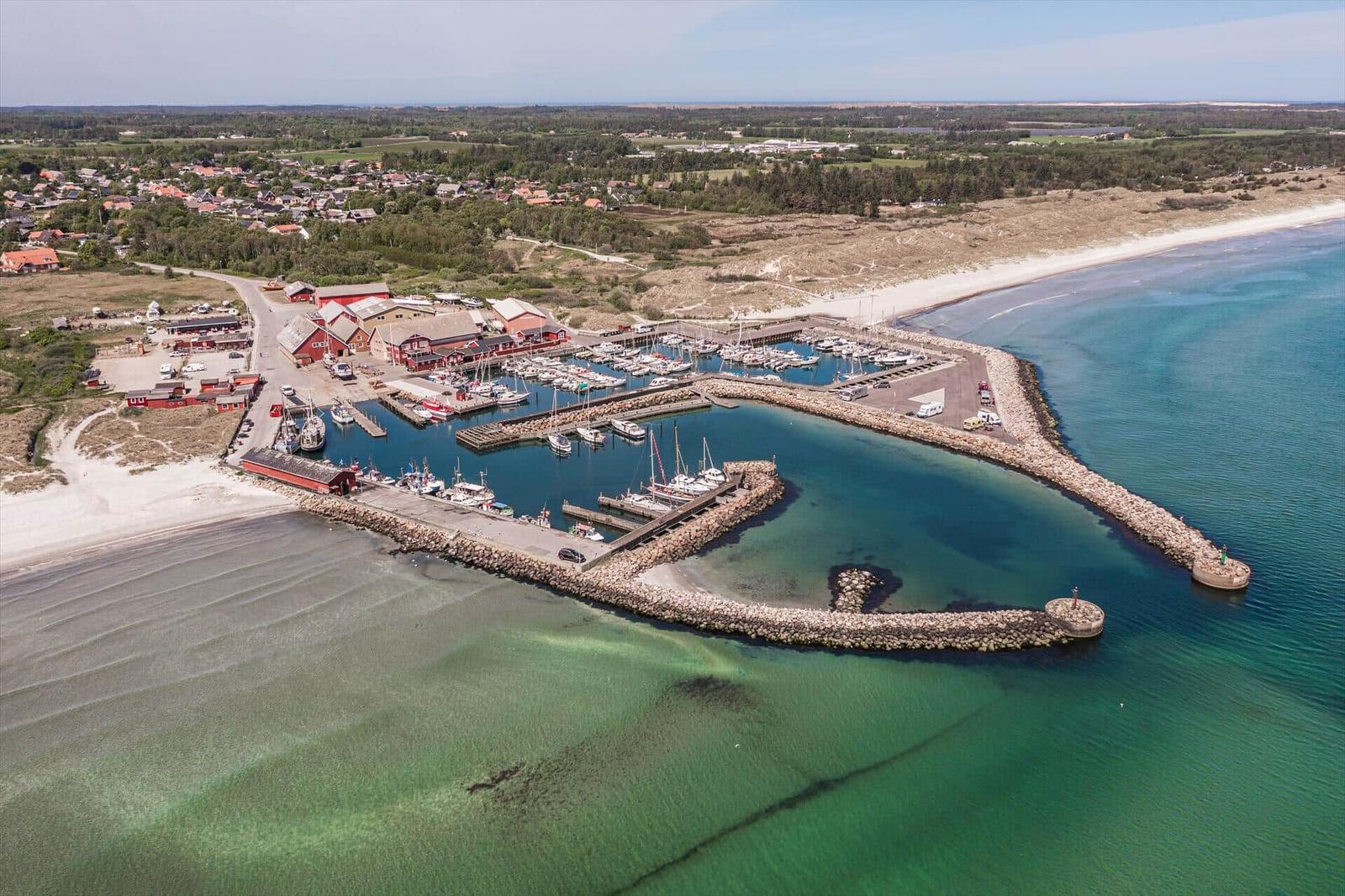 Harbor with boats, beach, and red buildings along the coast.