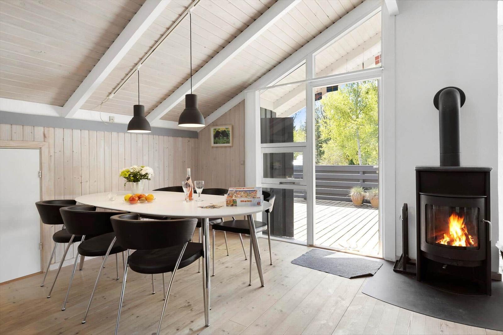 Dining area with table, chairs, and fireplace. Access to terrace with view of greenery.