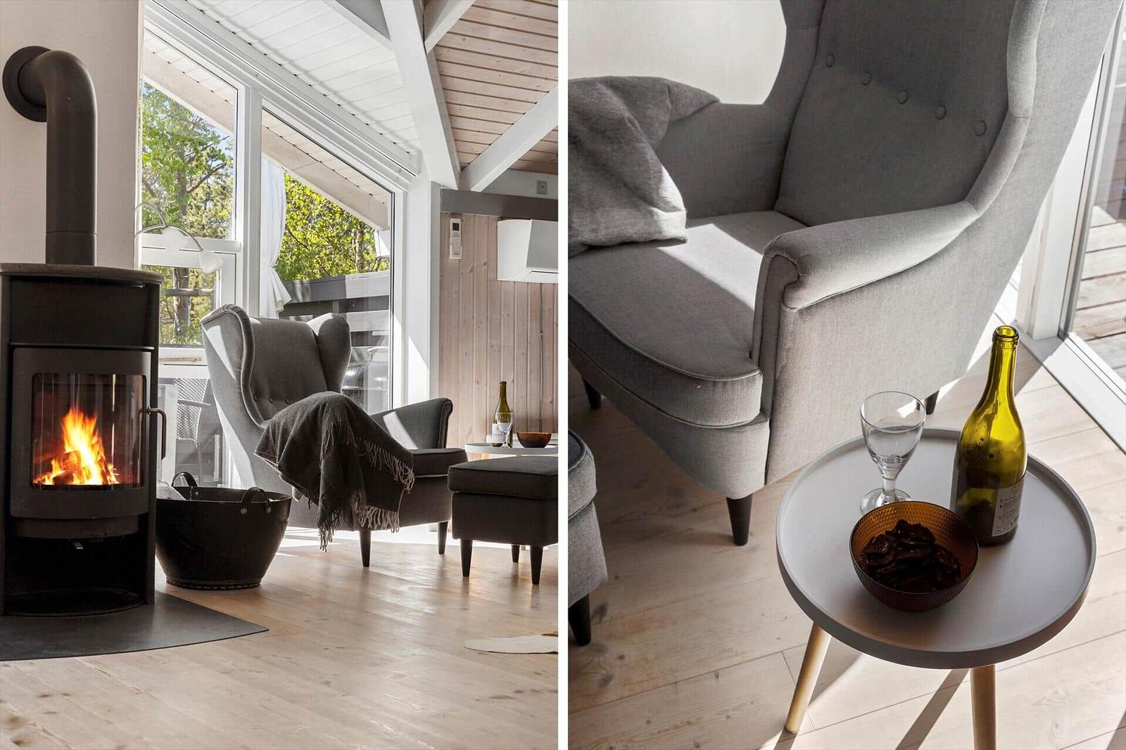 A room with a fireplace, gray armchairs, and wooden floor. On a table is a bottle and a glass.