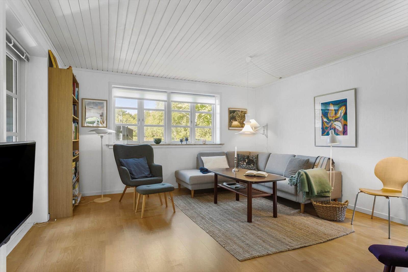 Wohnzimmer mit Sofa, Sessel und Tisch. Holzboden und weiße Wände.