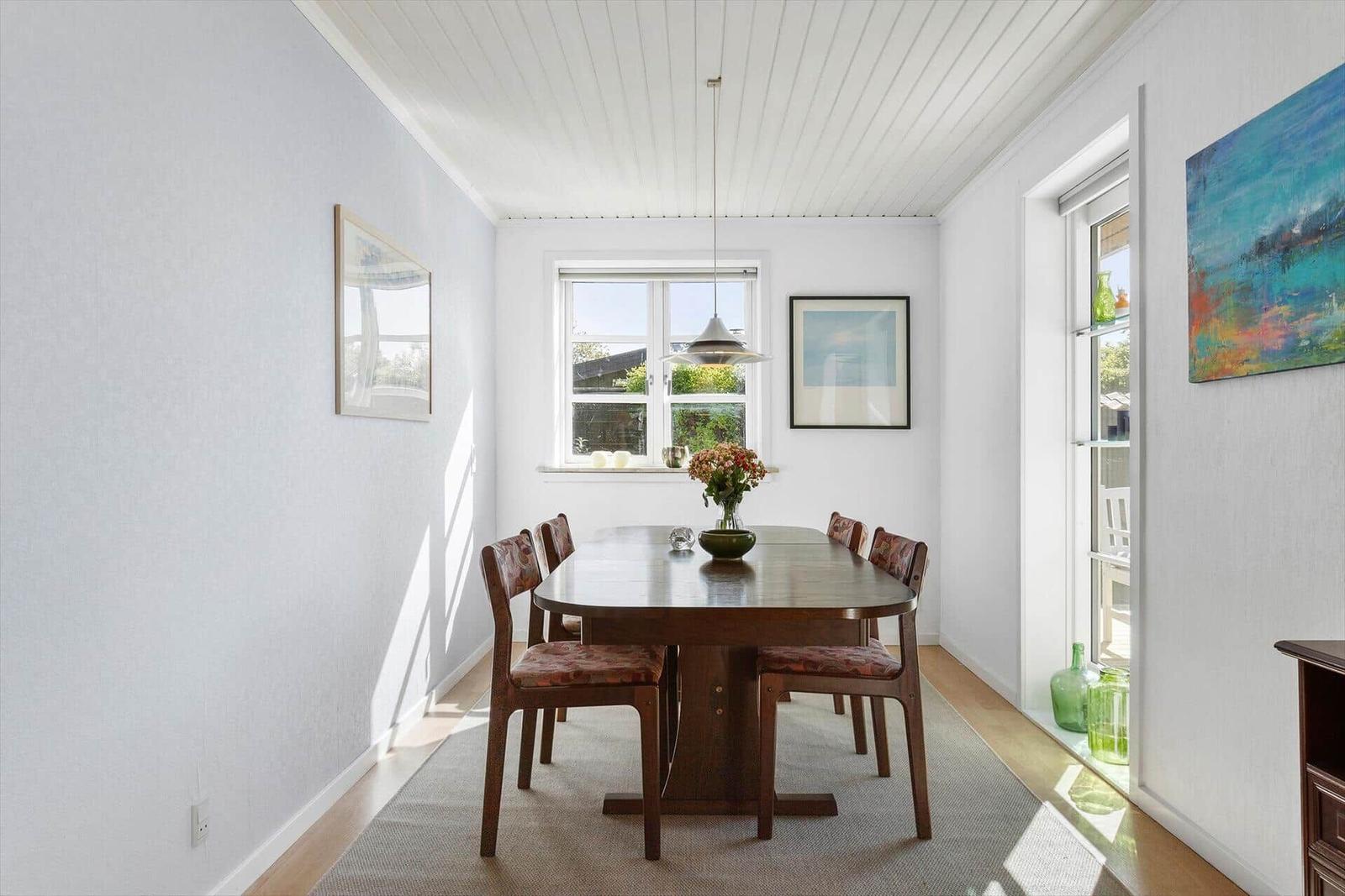 Esszimmer mit Holztisch, Stühlen und Fenster. Wandbild und Hängelampe.