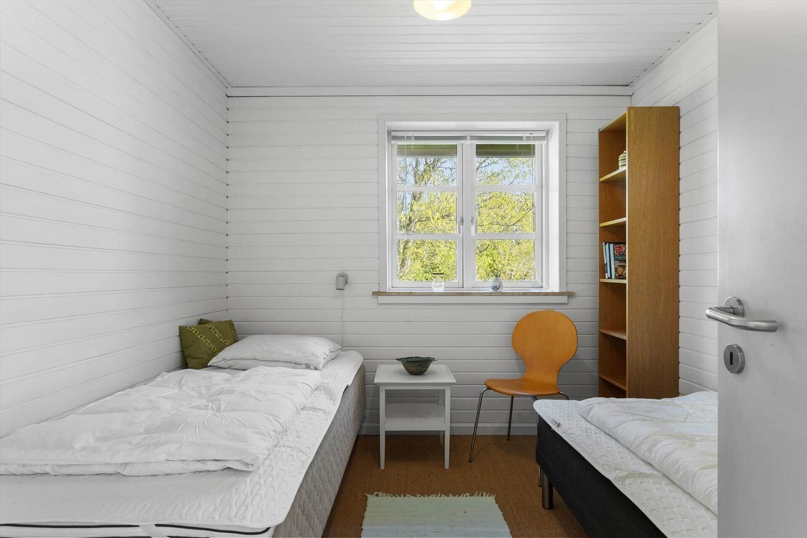 Zwei Betten, ein Fenster, ein Stuhl und ein Bücherregal in einem Raum mit weißen Wänden.