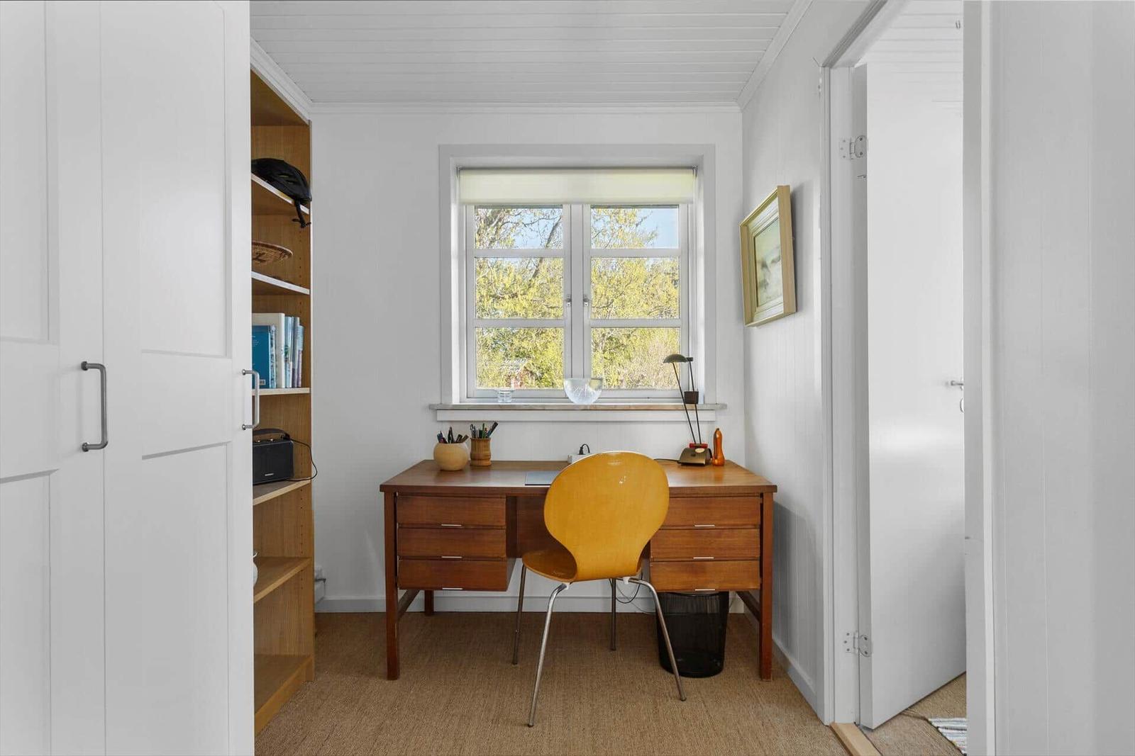 Schreibtisch mit gelber Stuhl und Fenster mit Blick auf Bäume.