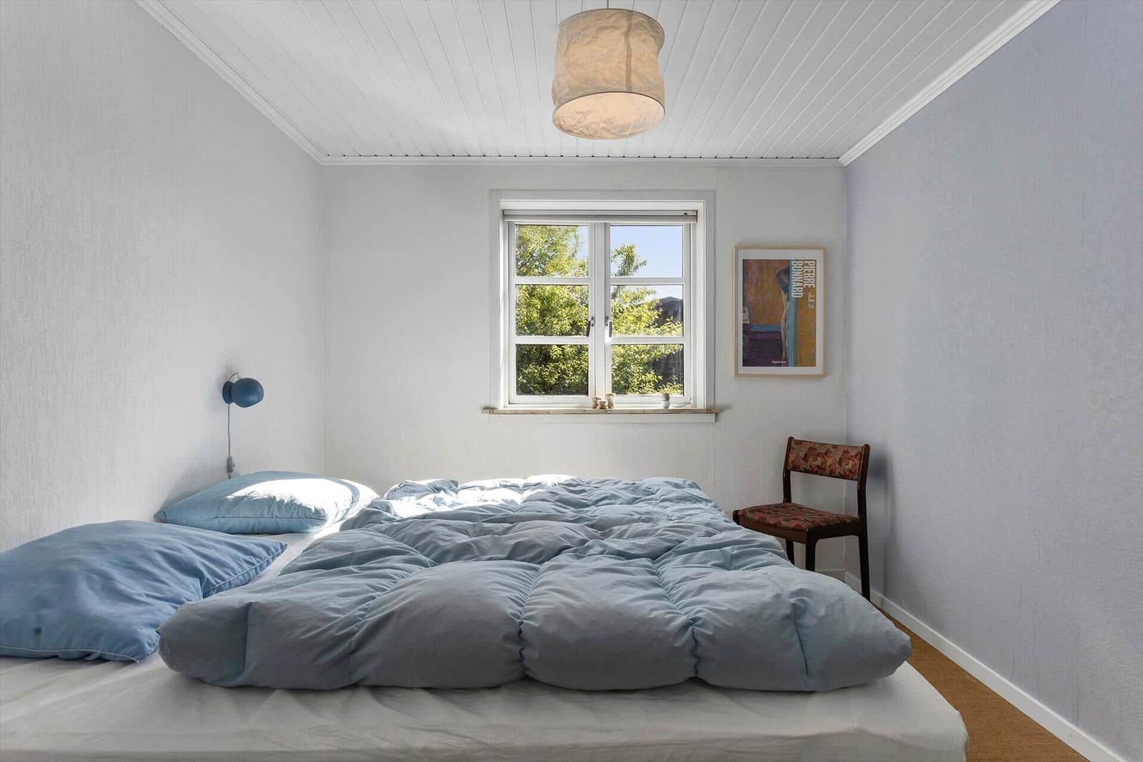 Schlafzimmer mit Bett, Fenster und Stuhl.