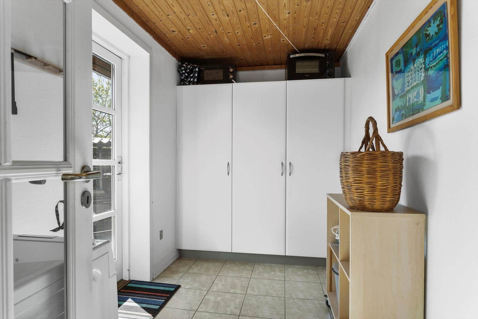 Eingangsbereich mit weißen Schränken, Holzdecke und Korb auf Regal.
