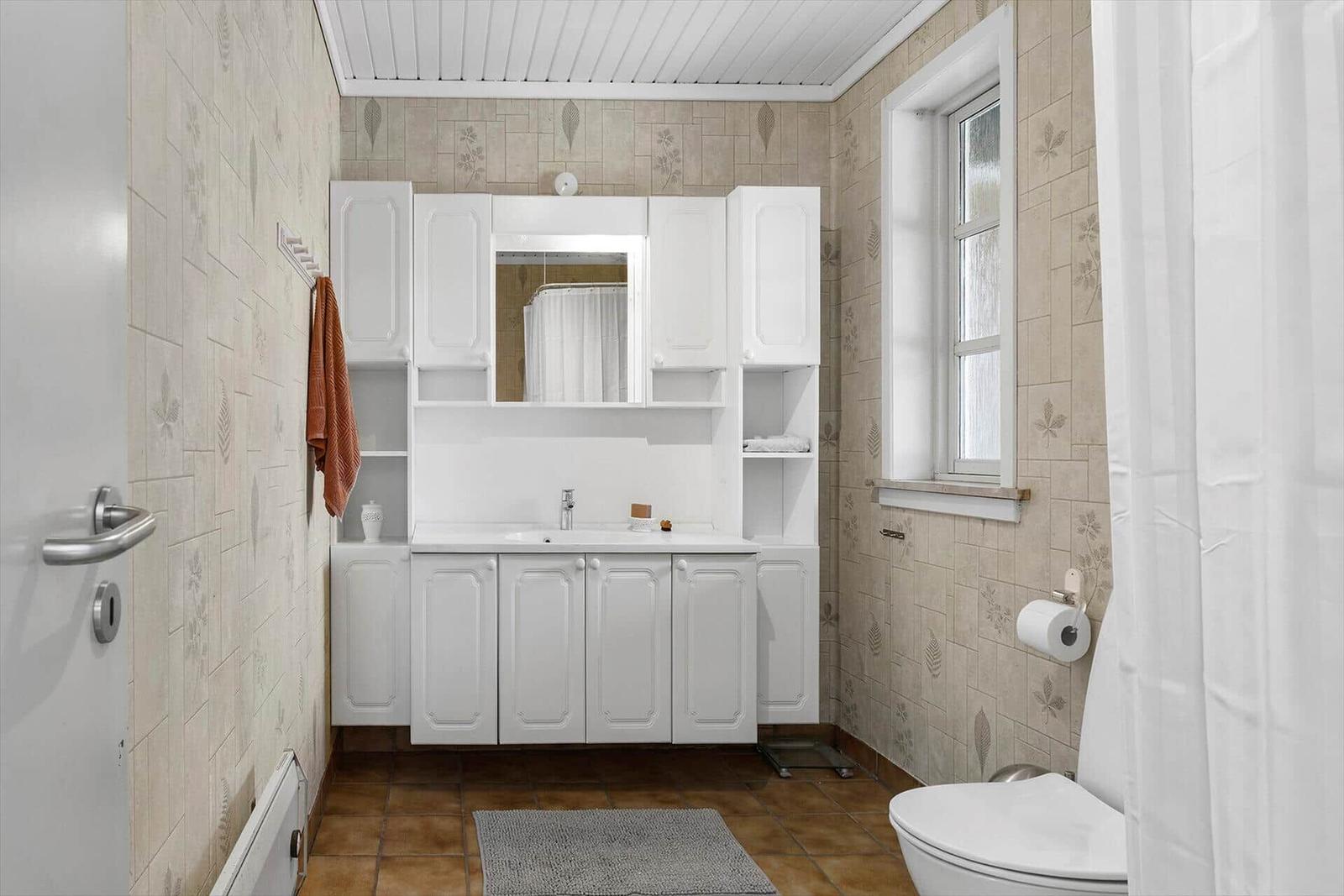 Badezimmer mit weißem Waschbecken, Spiegel, Toilette und Duschvorhang.
