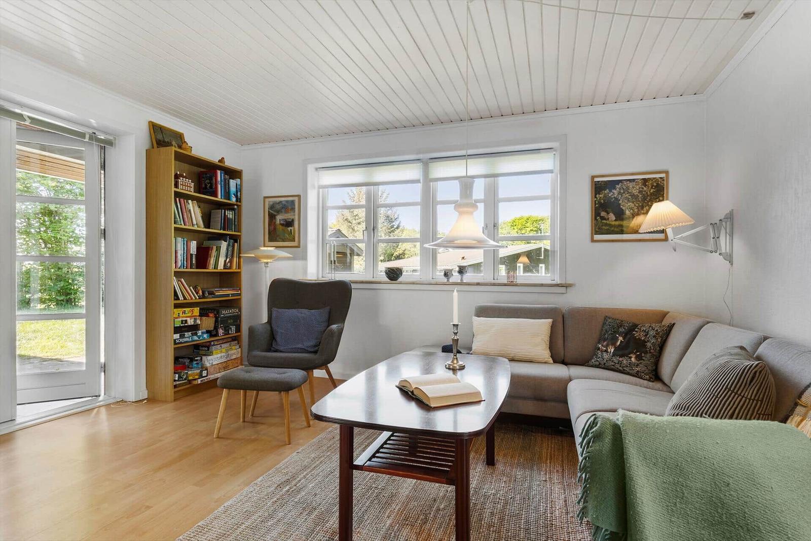 Wohnzimmer mit Sofa, Tisch, Stuhl und Bücherregal. Fenster und Tür zu Garten.